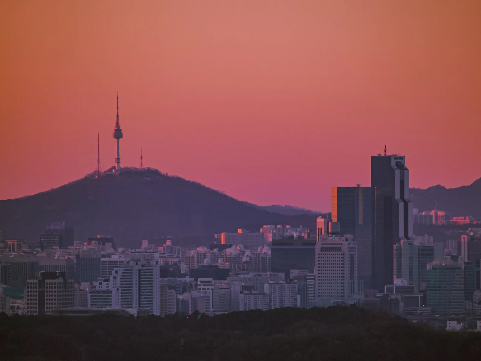 N Seoul Tower on a hill above the city skyline at sunset under a pink-orange sky